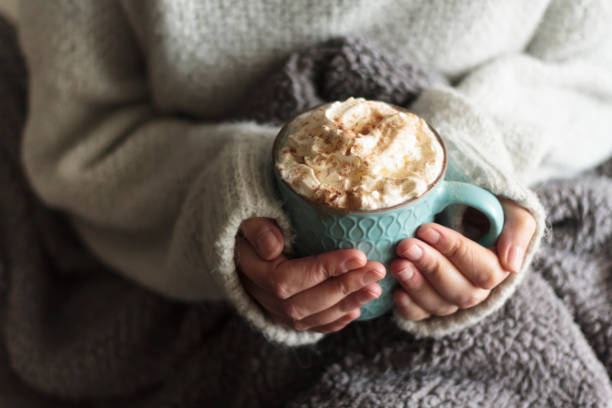 Woman with blanket warming her hands in mug of hot drink with whipped cream